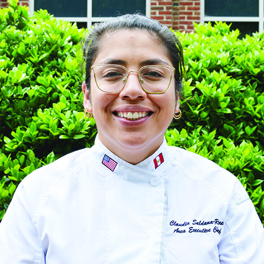 A female chef smiling and wearing a chef coat.