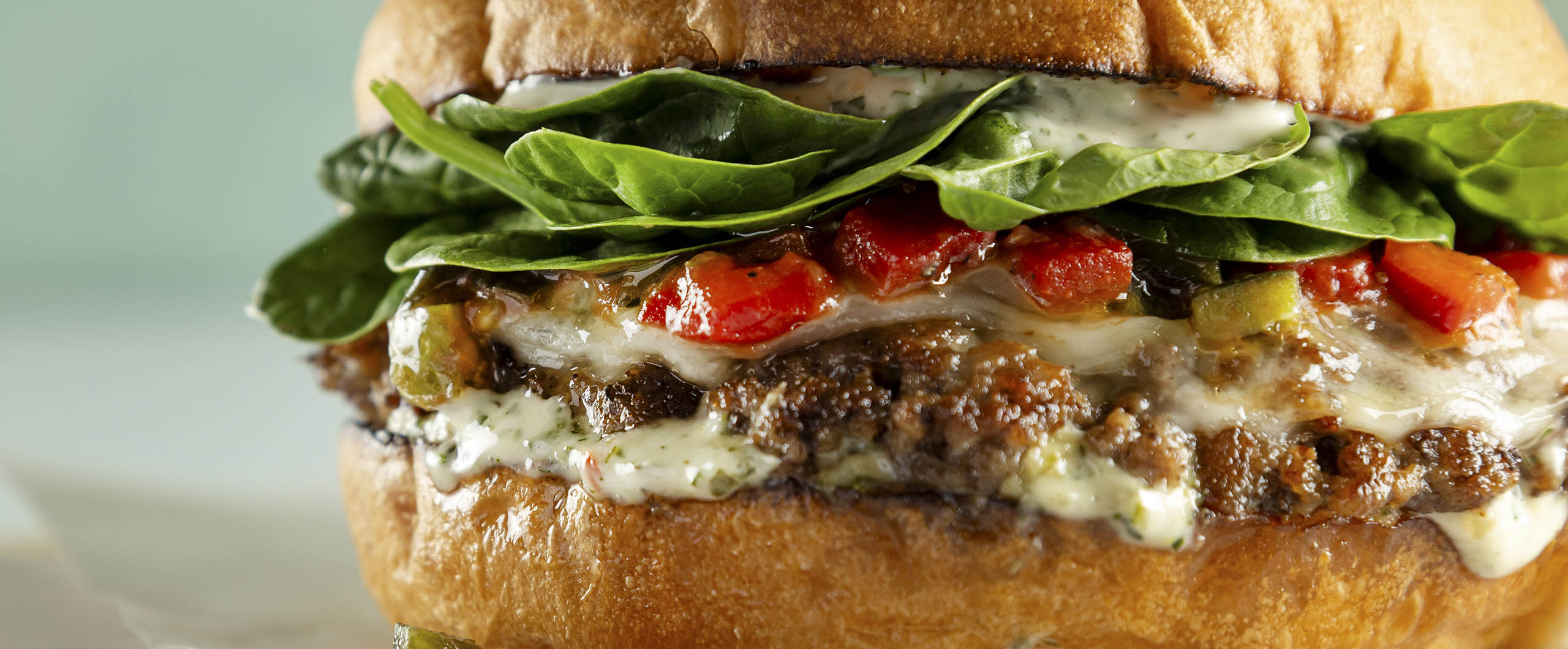 A burger featuring a Smashed burger with provolone, chimichurri mayonnaise, tomato pepper relish, baby spinach on a toasted Kaiser roll.